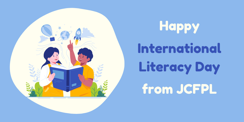 Banner celebrating International Literacy Day from JCFPL, featuring an illustration of two children reading a book together with imagery of a globe, rocket, and hot air balloons above them, set against a light blue background with the text on the right.